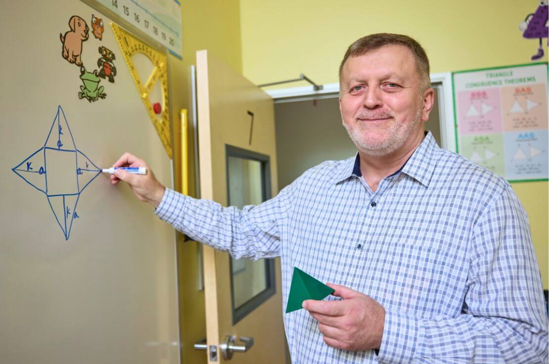 RSM teacher writing on whiteboard, holding pyramid